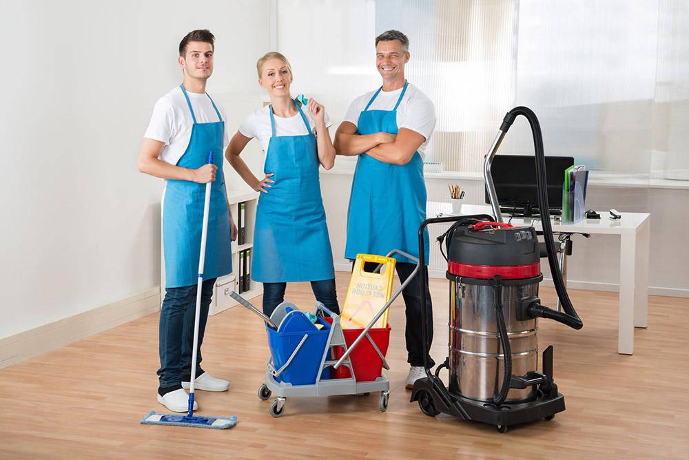 Happy Janitors With Vacuum Cleaner And Cleaning Equipments In Office